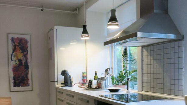A modern kitchen with white cabinets, a stainless steel range hood, pendant lights, and a window with a view of greenery. - City Apartment in Frederiksberg with 2 bedrooms sleeps 4 (Frederiksberg)