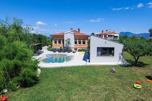 A modern house with a swimming pool, a separate building with large windows, and a well-maintained lawn.