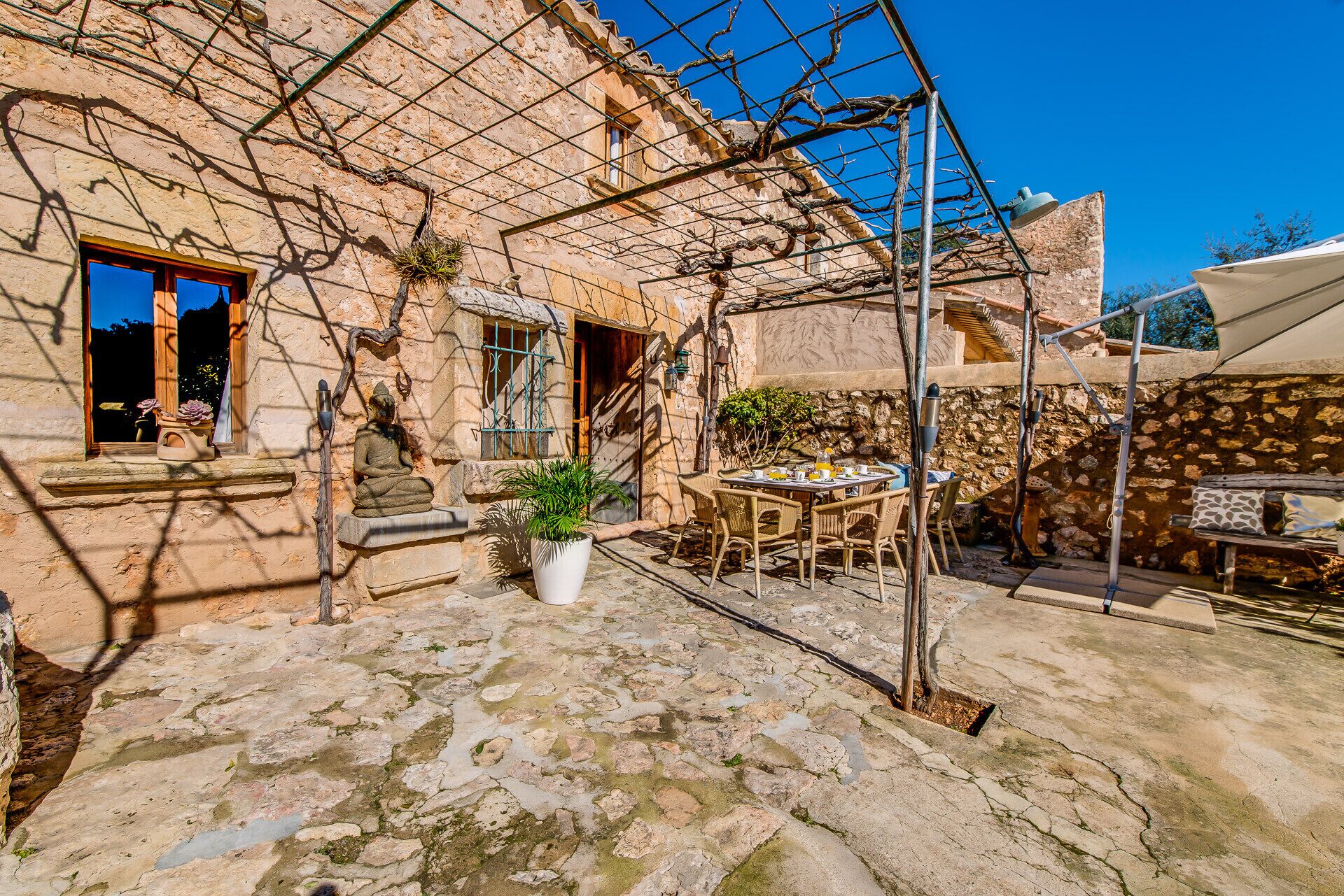 A stone courtyard with a table and chairs, a statue, and a potted plant.