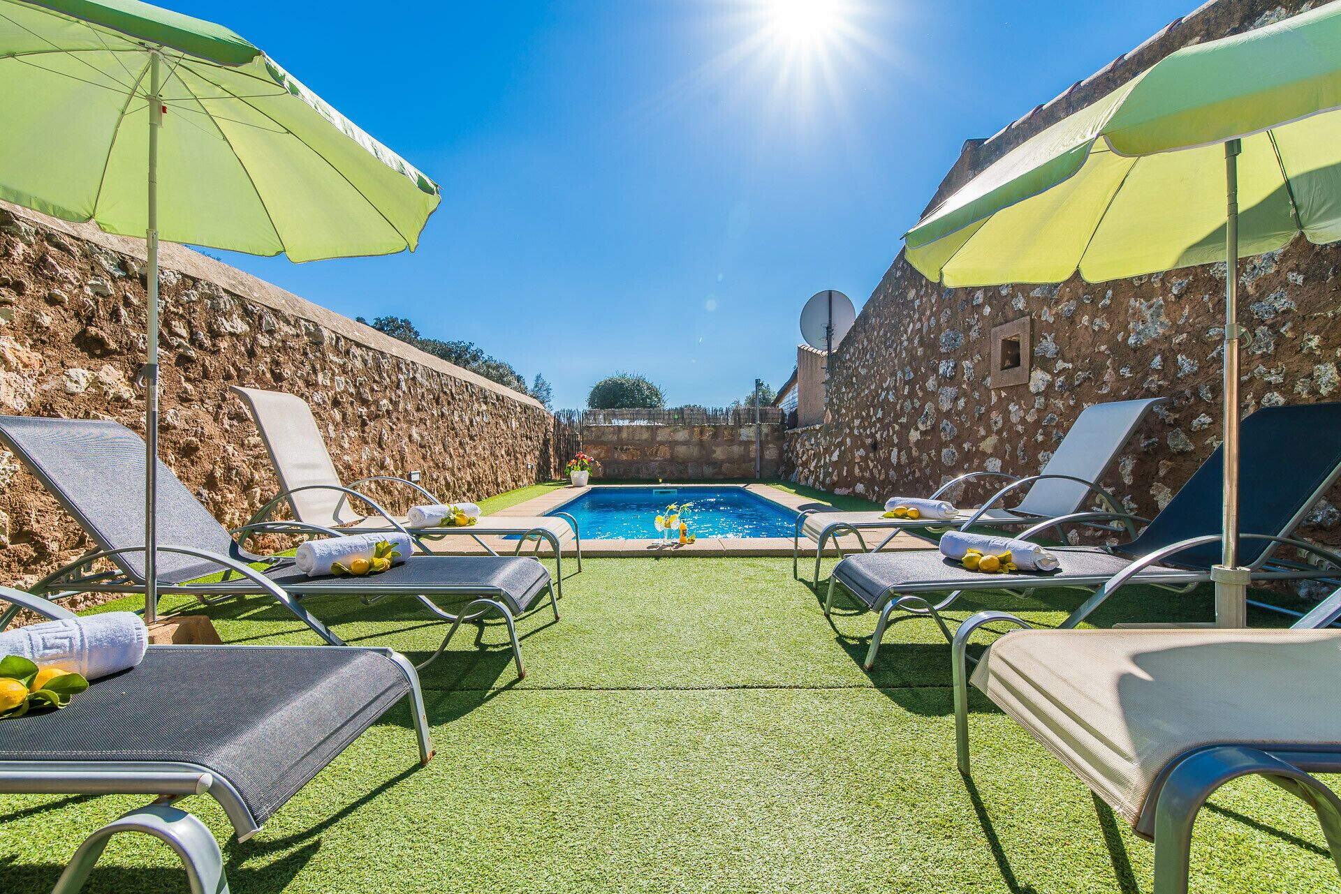 Zona de piscina con sillones de descanso y sombrillas, rodeada de muros de piedra.