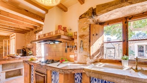A rustic kitchen with a stone wall, wooden beams, and a large window.