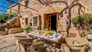 A rustic outdoor dining area with wicker chairs and a table set for breakfast.