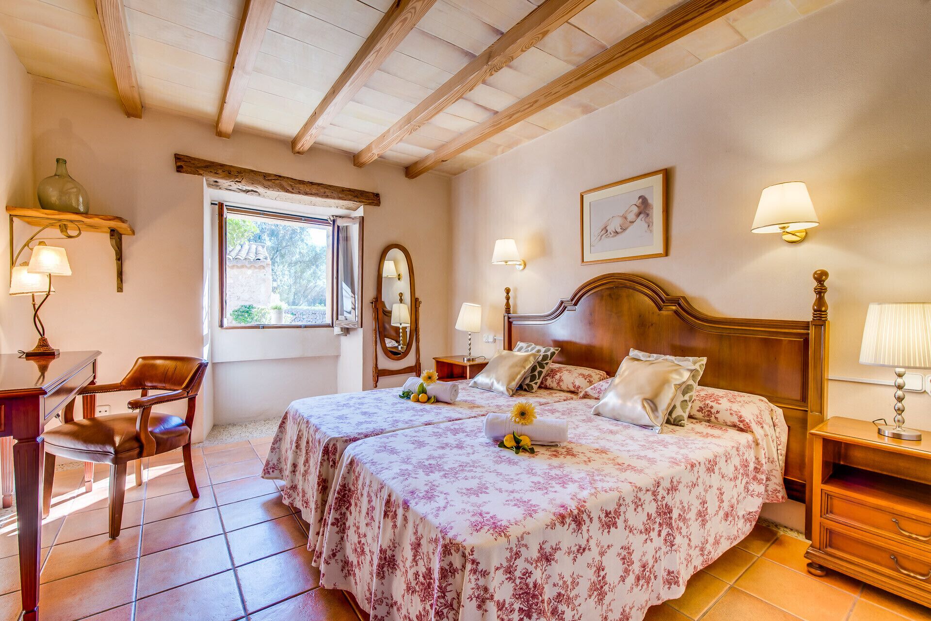 Un dormitorio con dos camas, una silla de madera, un escritorio y una ventana con vistas a zonas verdes.