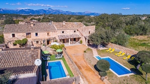 A villa with a swimming pool, outdoor seating, and a mountainous backdrop.
