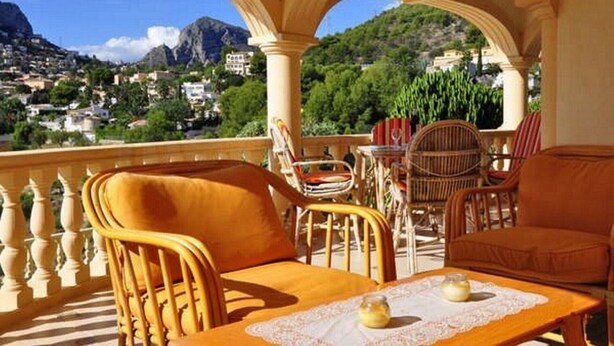 A balcony with wicker furniture, a table with a candle, and a view of a mountainous town. - Modern apartment: electricity, washing machine WIFI, bed linen, towels INCL. 4 p (Calpe)