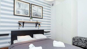Ein Hotelzimmer mit einem Bett, zwei gerahmten Bildern an der Wand, einem Nachttisch mit Lampe und einem osmanischen Hocker mit Zebramuster.