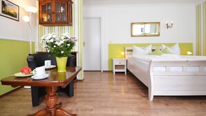 A hotel room with a bed, a bedside table, a chair, a dining table with a vase of flowers, and a mirror on the wall. - Cozy vacation apartment in Heringsdorf with terrace - 400 m to the beach (Seebad Heringsdorf)