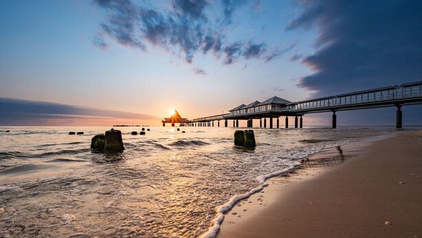 A beach with a pier extending into the water, featuring a series of buildings and a walkway.