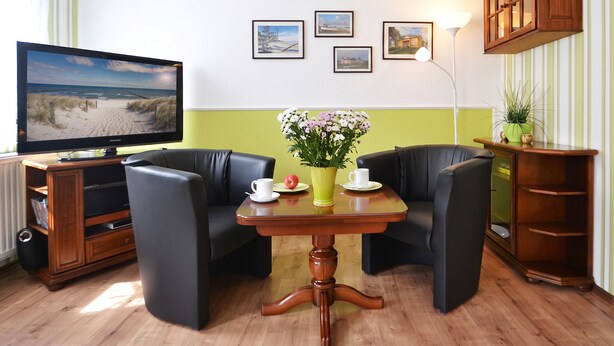 A room with a television, two armchairs, a small table with a vase of flowers, and a cabinet. - Cozy vacation apartment in Heringsdorf with terrace - 400 m to the beach (Seebad Heringsdorf)