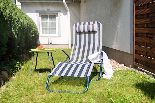 A striped lounge chair with a towel, a glass of water, and a slice of watermelon on a small table in a grassy outdoor area. - Cozy vacation apartment in Heringsdorf with terrace - 400 m to the beach (Seebad Heringsdorf)