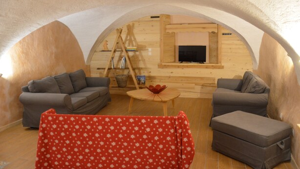 Un cuarto ático acogedor con dos sofás grises, una mesita de madera y un mantel rojo estampado.