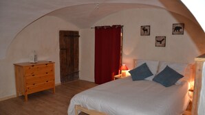 Un dormitorio con cama de madera, cómoda, cortina roja y decoración en la pared.