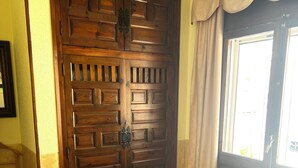 A bedroom with a wooden wardrobe, a bed with white bedding, a window with curtains, and a tiled floor.