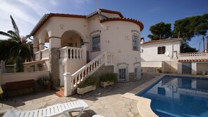 A house with a swimming pool, stone patio, and a staircase leading to an upper level.