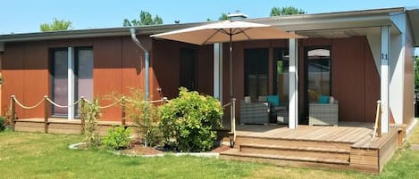 Un bâtiment moderne doté d’un espace extérieur aménagé avec une terrasse couverte, une plateforme en bois et une clôture en treillis métallique.