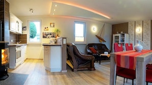 Una sala de estar moderna con chimenea, un comedor con sillas rojas y una cocina con estufa.