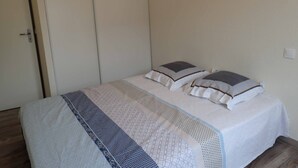 Een enkel bed met een wit- en blauwe sprei, twee kussens en een houten vloer.