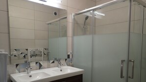 Een moderne badkamer met twee wasbakken, een douchecabine met glazen wanden en een spiegel.