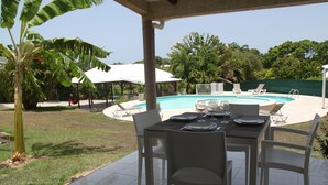 An outdoor pool area with a covered patio, dining table, and chairs.