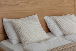 Una cama con cabecera de madera, ropa de cama blanca y almohadas con textura.