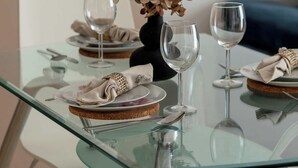 A glass-top dining table with plates, cutlery, and wine glasses set for two.