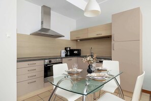 Une cuisine moderne avec une table à manger en verre, des chaises blanches et une hotte de cuisine en acier inoxydable.