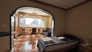 Quarto com cama, escrivaninha e cadeira. Janela com vista para uma montanha.