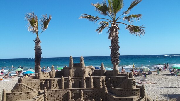 Uma praia com um castelo de areia grande e palmeiras.