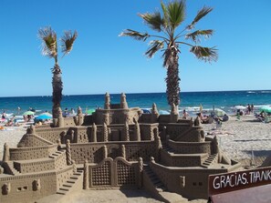 Ein Strand mit einer großen Sandburg und Palmen.