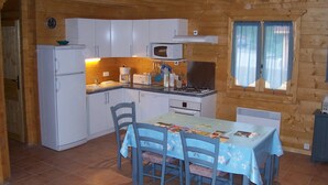A compact kitchen with white cabinets, a microwave, and a dining area with a table and chairs. - Gîtes of 75m², sleeps 6 with swimming pool (JURA) (Commenailles)