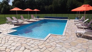 A rectangular swimming pool with a stone tile deck, surrounded by lounge chairs and orange umbrellas. - Gîtes of 75m², sleeps 6 with swimming pool (JURA) (Commenailles)