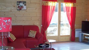 A cozy room with a red sofa, a glass table, a TV, and a door leading to a scenic outdoor area. - Gîtes of 75m², sleeps 6 with swimming pool (JURA) (Commenailles)