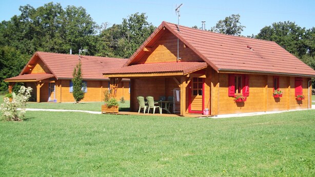A wooden cabin with a red roof, a covered porch, and a small outdoor seating area. - Gîtes of 75m², sleeps 6 with swimming pool (JURA) (Commenailles)