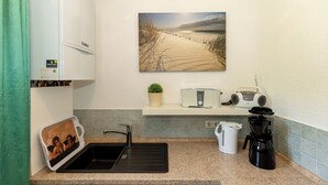 Una cocina con un lavamanos, encimera, tostadora, radio, cafetera y un cuadro de una playa.