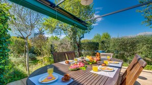An outdoor dining area with a wooden table, chairs, and a view of trees and a body of water. - Country house Can Flauta with pool in Mallorca (Selva)