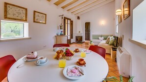 A dining area with a round table set for breakfast, a fireplace, and a sofa in the background. - Country house Can Flauta with pool in Mallorca (Selva)