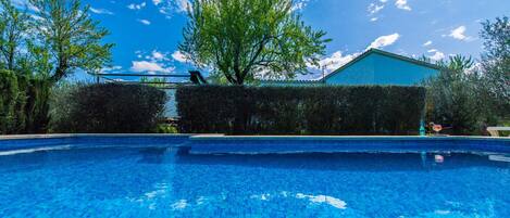 A swimming pool with clear blue water, surrounded by greenery and a building with a blue roof.