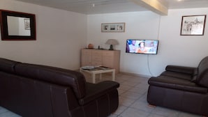 Ein Wohnzimmer mit zwei braunen Ledersofas, einem Holzschrank, einem kleinen Tisch und einem an der Wand befestigten Fernseher.
