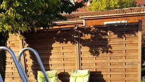 A swimming pool with metal ladders, surrounded by a wooden deck and a wooden fence.