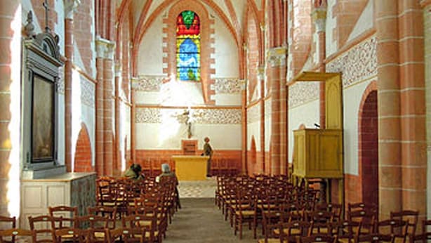 An interior of a church with high vaulted ceilings, a central stained glass window, and rows of wooden pews.