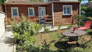 A wooden house with a balcony, a round table with chairs, and a red chair.