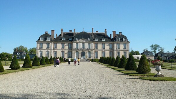 A large, historic building with a symmetrical facade, multiple chimneys, and a gravel driveway.