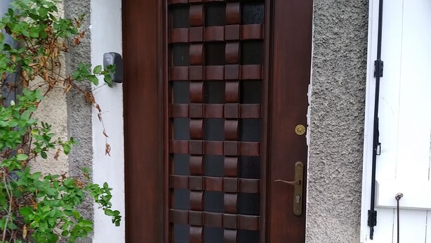A brown door with a decorative grid pattern, a small step leading to the entrance, and a utility box labeled "AUDRAN FRANÇ" on the wall.