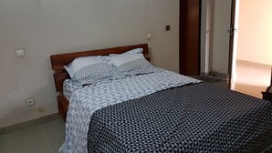 A bedroom with a bed, two wall-mounted lights, a wooden door, and a tiled floor.