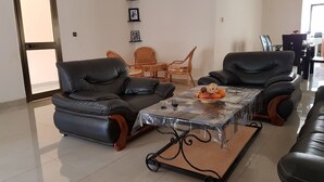A living room with two black leather sofas, a glass coffee table with fruit, and a dining area with wicker furniture.