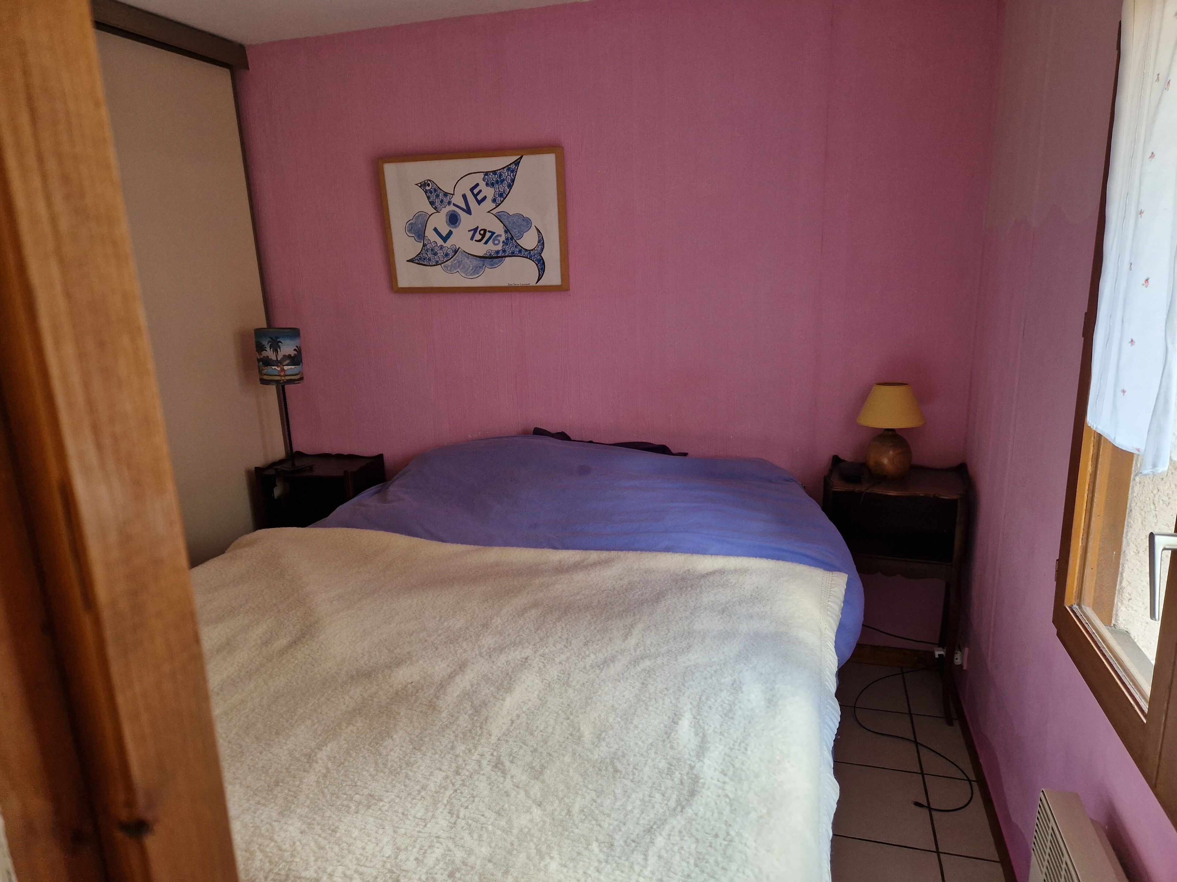 Een slaapkamer met een bed, nachtkastje, lamp en een decoratie aan de muur.