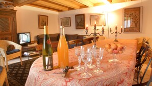 Una sala de estar acogedora con techo de madera, una mesa con copas de vino y una botella, y un televisor al fondo.