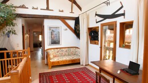 Una sala de estar acogedora con una escalera de madera, un sofá, una mesa de comedor con un ordenador portátil y una alfombra roja estampada.