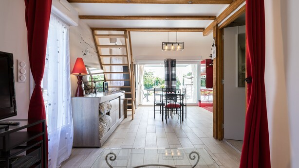 A spacious room with a wooden ceiling, a dining area with chairs and a table, and a staircase leading to another level. - SMALL RELAXATION CORNER (Seyresse)