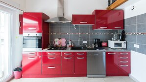 A modern kitchen with red cabinets, a stainless steel range hood, a microwave, and a dishwasher. - SMALL RELAXATION CORNER (Seyresse)